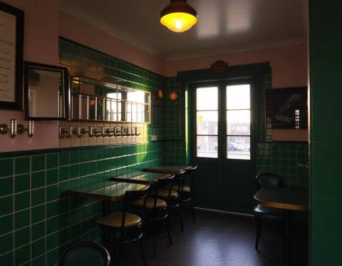 Small corner café interior with green tiles and brass fittings, warm evening light, empty and quiet, architectural photo
