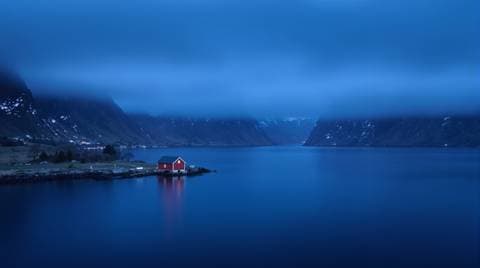 Norwegian fjord under low fog, a single red boathouse on the shore, cold blue palette, landscape photography