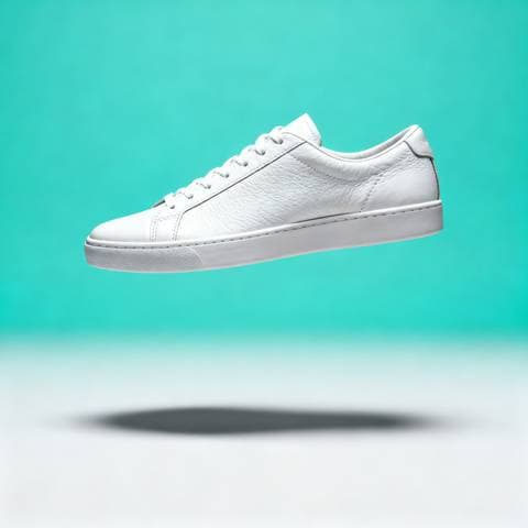 White leather sneaker floating against a mint background, soft shadow beneath, clean studio product shot, catalogue styl
